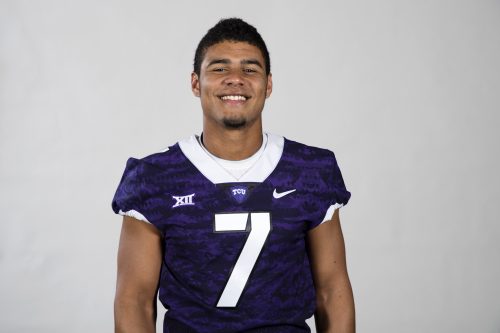 Quarterback Kenny Hill stands smiling in front of a white background with his purple jersey on.