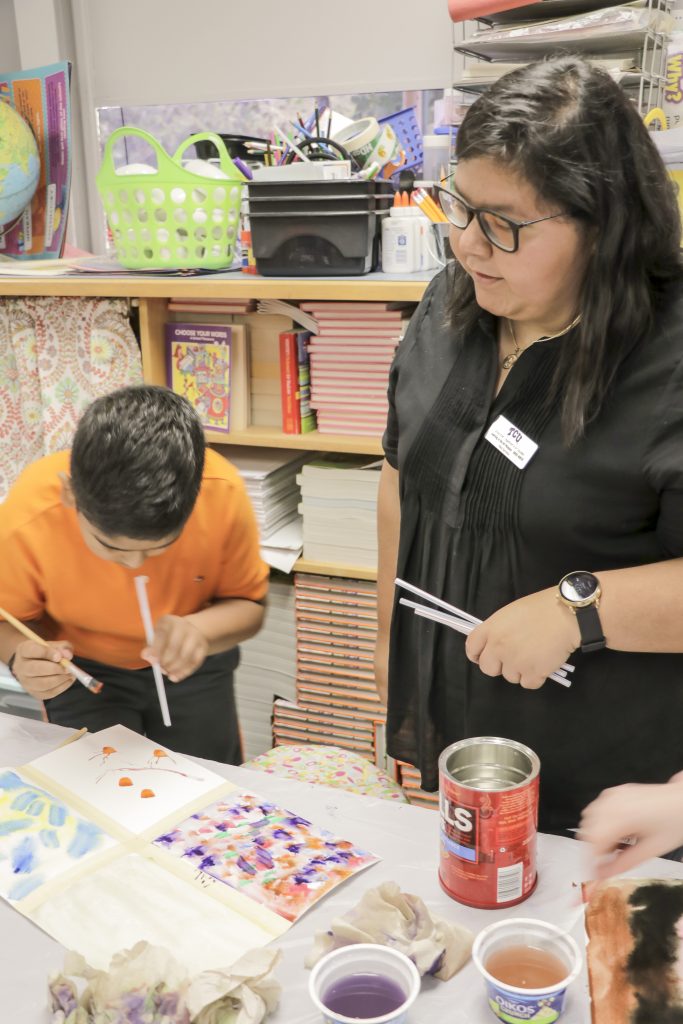 TCU student Maria Barrientos (right) helps a student create abstract expressionistic shapes by blowing on fresh watercolor through a plastic straw. Photo courtesy of Jenny Moore
