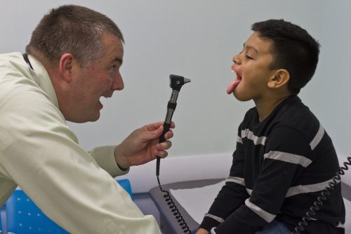 Dr. Donald Beam looks inside a young boys mouth with an otoscope.