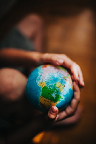 Hands hold a small world globe.