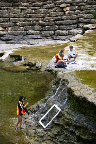 Nathania Davis, a junior psychology and criminal justice major, uses a picture frame to create scenes in the river as TCU art students use a variety of media to create art work at Airfield Falls Conservation Park. Photo by Rodger Mallison