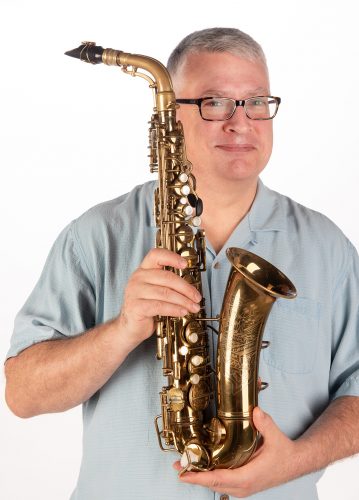 Jeffrey Todd stands in front of a white background holding a saxophone.