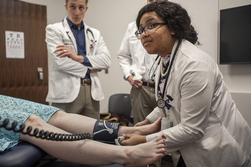 Charna Kinard practices an examination on a patient. She places a blood pressure cuff around a patient's ankle.
