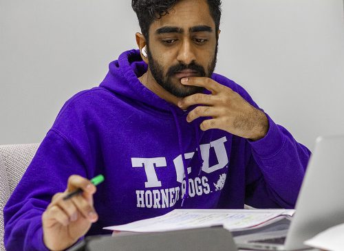 Dilan Shah sits in front of his laptop and a stack of notes. He has one hand on his chin and the other hand holds a pen.