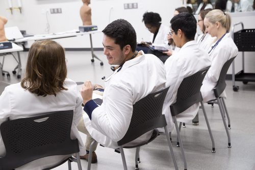 Edmundo Esparza sits with classmates wearing white coats.
