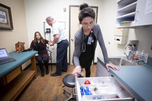 Ive Mota Avila opens a supply drawer inside a hospital examination room.