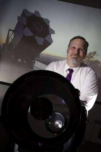 Dr. Peter Frinchaboy, Associate Professor of Physics and Astonomy in TCU's College of Science and Engineering, photographed by Rodger Mallison, September 28, 2020. In the foreground is a small telescope; the backdrop is a projected photo of the Sloan Foundation telescope at Apache Point Observatory in New Mexico.