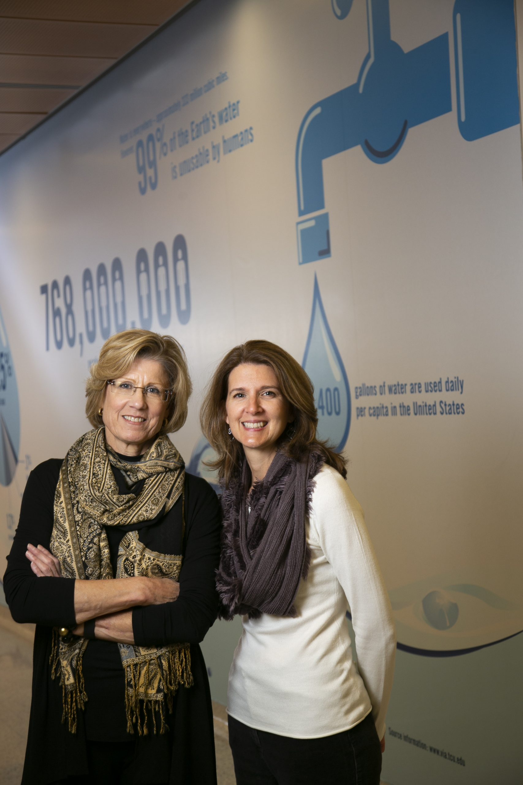 Sharon Canclini and Gina Alexander pose with a graphic about water use in Rees-Jones Hall. A recent paper they co-authored explored ways to simulate the health care response to an outbreak of waterborne disease.