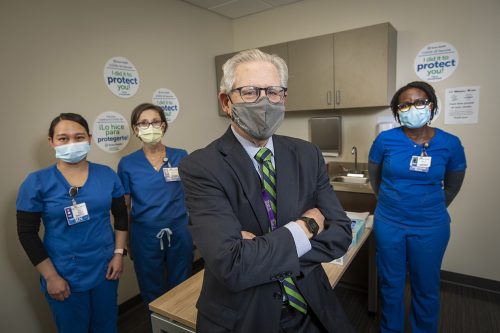 A photo of Barclay Berdan in a suit and PPE mask with three female nurses in scrubs.