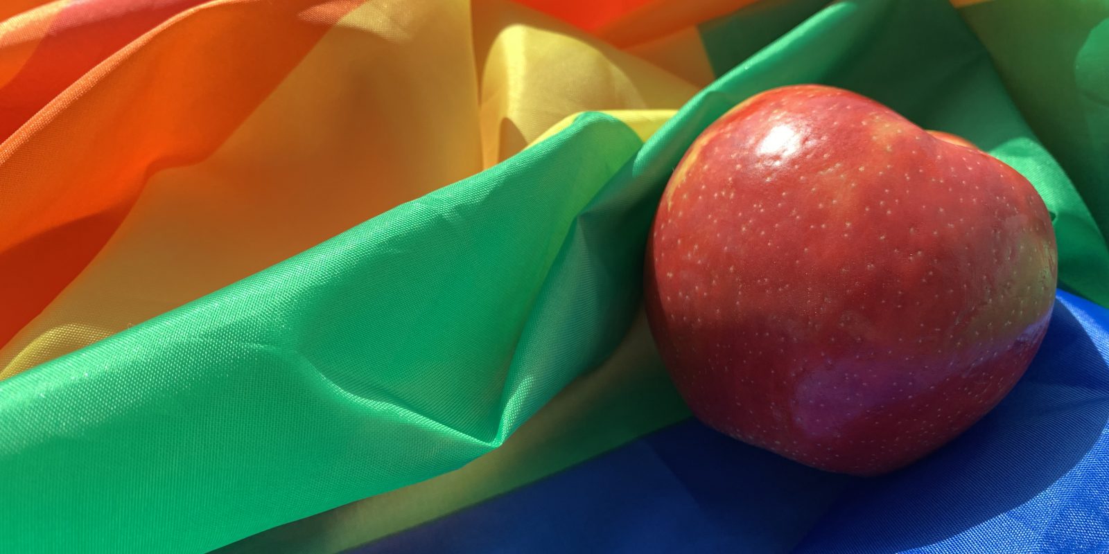 A bright red apple nestled on top of a rainbow LGBTQ+ pride flag.