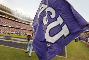 A TCU Ranger runs with a big TCU flag across the TCU Football field.
