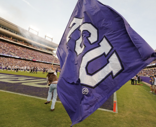 A TCU Ranger runs with a big TCU flag across the TCU Football field.