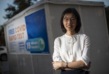 Jie Zhuang, assistant professor of communications studies is researching the acceptance of Covid vaccine in the African-American community. She is posing at a sign, in Fort Worth, advertising free Covid testing.