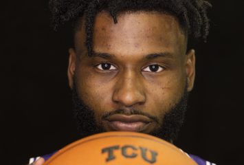 Mike Miles in a purple jersey holds out an orange basketball with "TCU" lettering