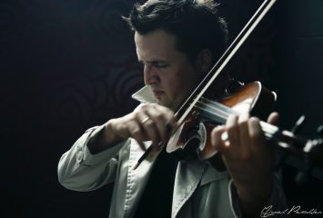 Man in deep concentration plays a stringed instrument before a dark background.