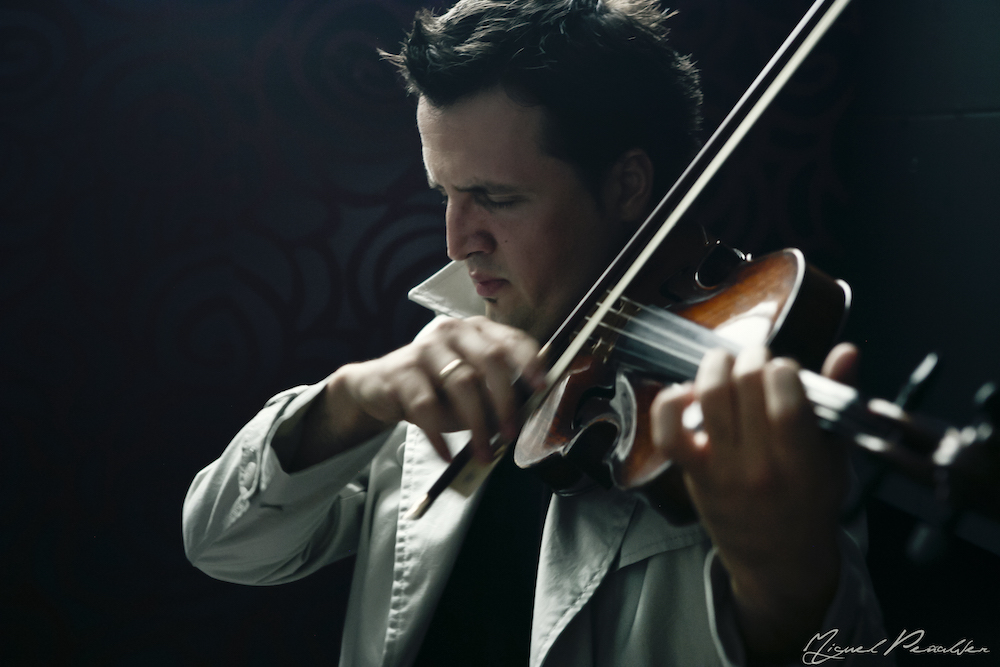 Man in deep concentration plays a stringed instrument before a dark background.