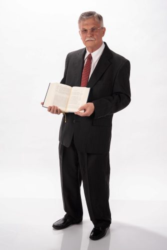 Man stands, holding open bible. 