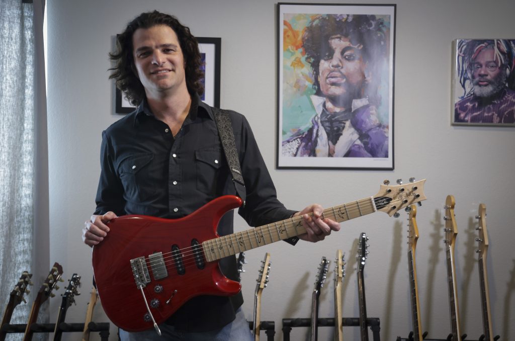 Feb. 27, 2024. In his home studio in Fort Worth, Texas, Grammy winning guitarist and composer Mark Lettieri '05 holds a red version of the “Fiore” model Paul Reed Smith guitar he designed for the company. (Photo by Ralph Lauer)