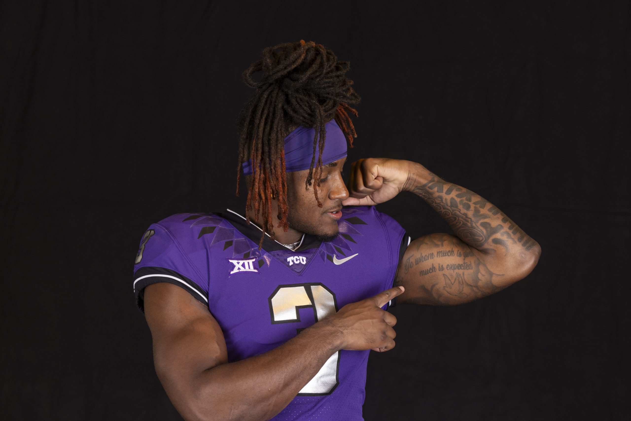 TCU wide receiver Savion Williams, wearing a purple Horned Frogs football jersey, flexes his left bicep as he points to it with his right index finger.