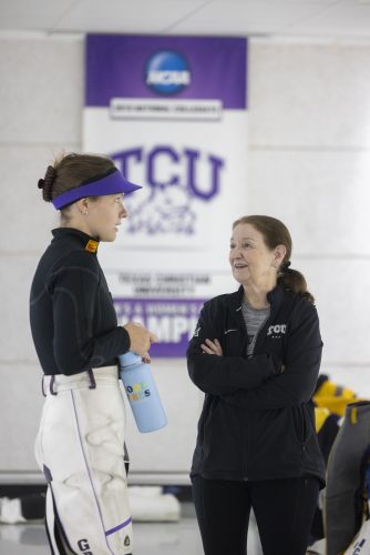 Coach Karen Monez, right, and Stephanie Grundsöe speak to one another during an October 2023 NCAA Rifle match at TCU. An NCAA Championship banner, with a TCU Horned Frog logo plastered across its center, hangs on the wall in the background.