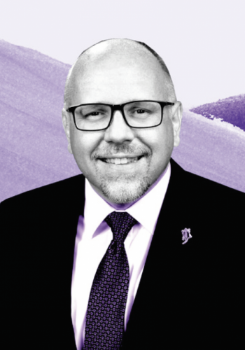 Image of Mike Caldwell, clad in a shirt, tie and jacket, set against a background consisting of three different shades of purple.