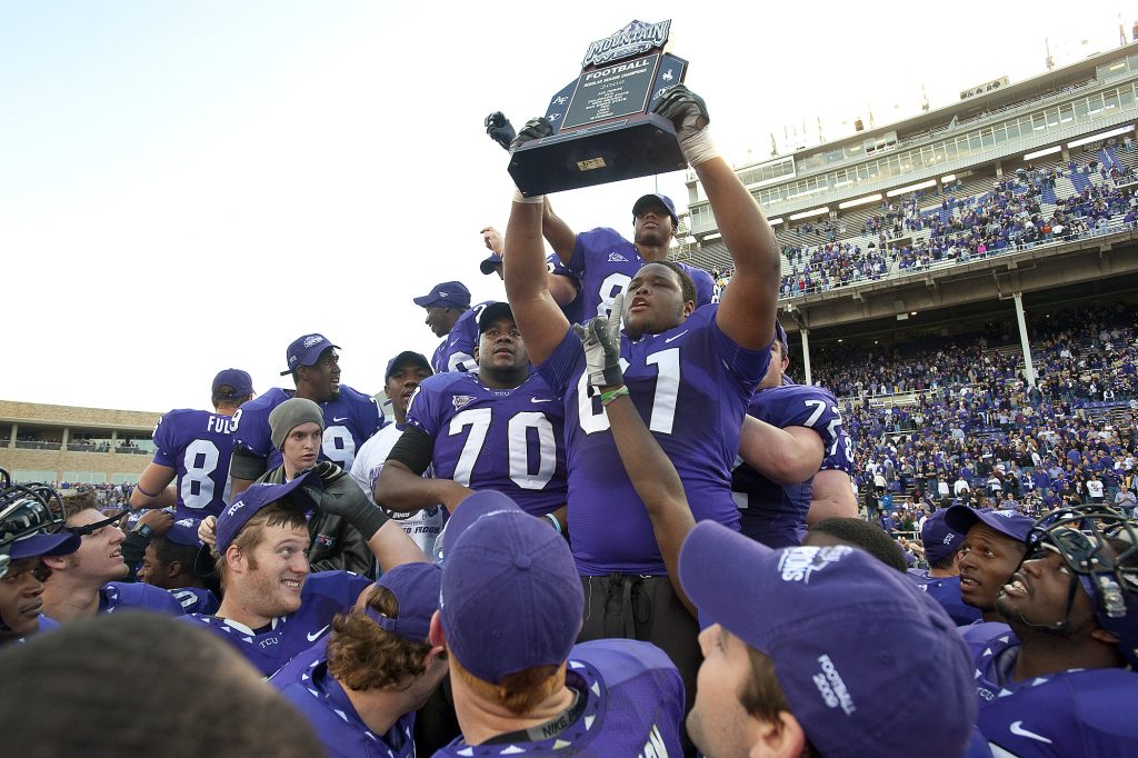 Photo of Horned Frogs football players gathering around a TCU student-athlete who is hoisting the 2009 Mountain West Conference championship trophy. 