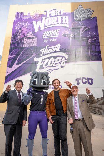 Photograph of President Daniel W. Pullin, SuperFrog, designer Trevor Scott ’22 and Chancellor Victor J. Boschni, Jr. holding up the TCU hand sign as they stand in front of Scott's TCU mural in downtown Fort Worth.