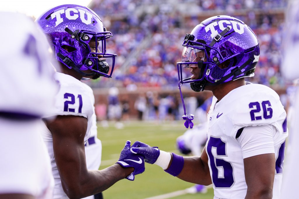 Photograph of TCU student-athletes Bud Clark and Jeremy Payne sharing a handshake during the Horned Frogs' Sept. 21 road football game at SMU. Clark and Payne wear TCU's white road football uniforms and purple helmets. 