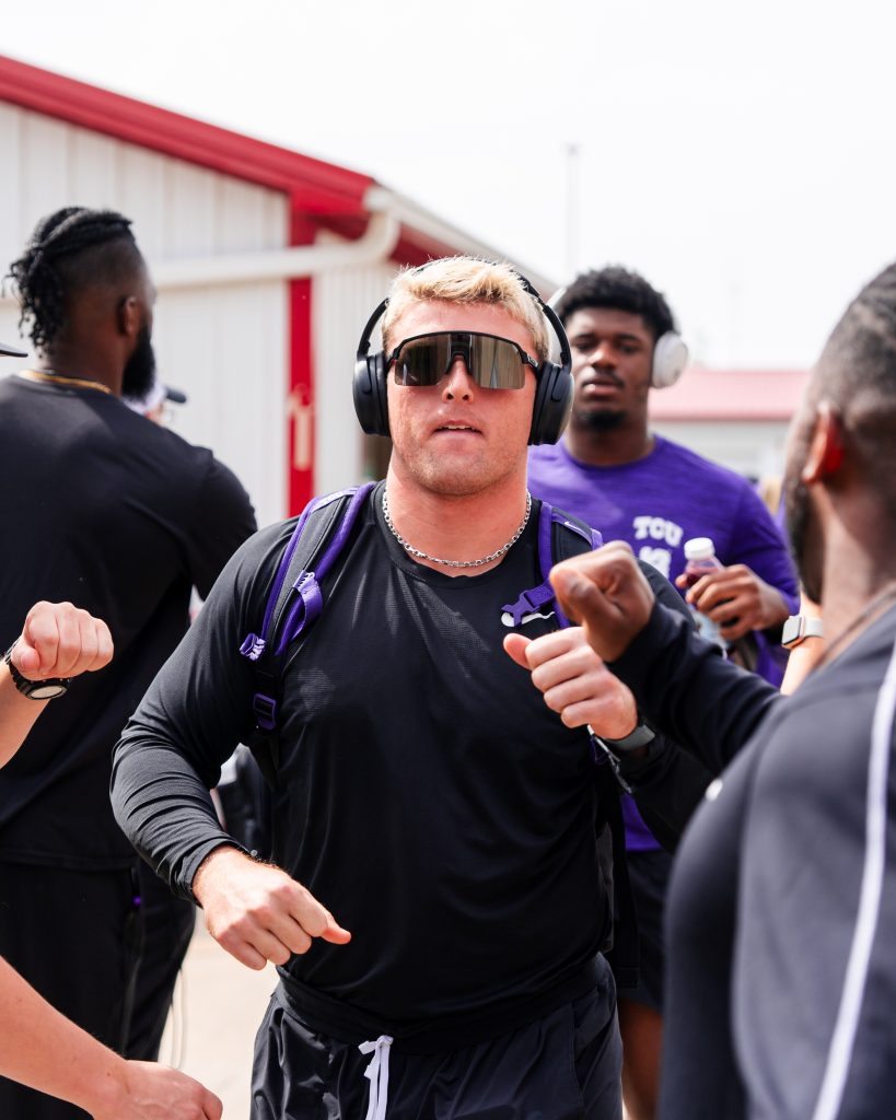 Photograph of TCU linebacker Johnny Hodges fist-bumping teammates and coaches after he and the team arrived in Kansas City. Hodges is wearing black headphones, black sunglasses and a black T-shirt.