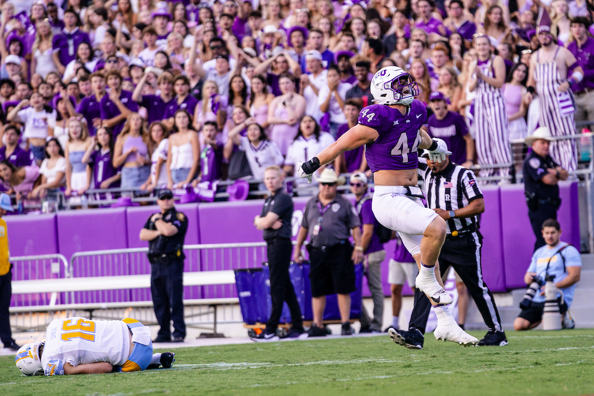 Photograph of TCU linebacker Cooper McDonald celebrating by leaping into the air during the Horned Frogs' 45-0 win against Long Island University on Saturday, Sept. 7, 2024. An LIU player lays on the ground in the background as the purple-cladded crowd celebrates in the stands.