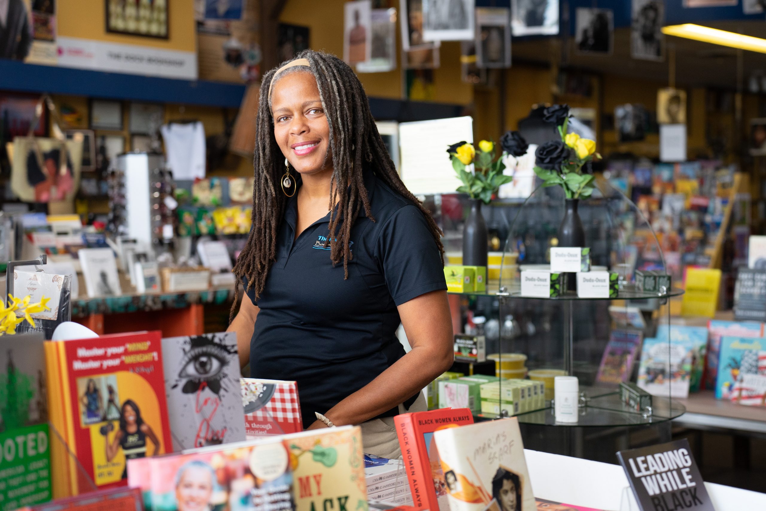 Smiling person in a black polo shirt standing in a bookshop, surrounded by books on tables and shelves.