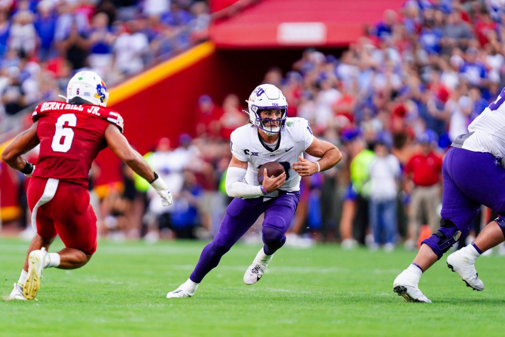 Photograph of TCU quarterback Josh Hoover, wearing a white football helmet, white jersey and purple pants, running on the field at Arrowhead Stadium during a 2024 college football game against the Kansas Jayhawks.