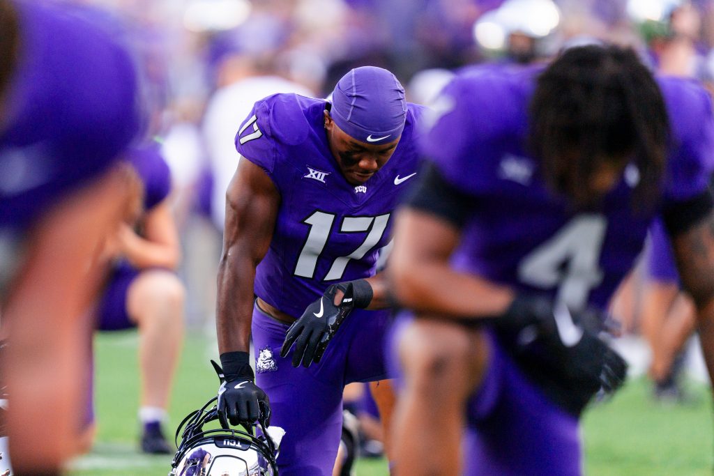 Photograph of TCU football players in purple uniforms kneeling in prayer on the field before the team's game against Houston on October 4.