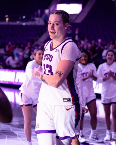 Photograph of TCU women's basketball player Prince running through a tunnel of her teammates as she steps onto the court at Schollmaier Arena on the Texas Christian University campus. She is wearing TCU's home white uniform with purple lettering and piping, and red accents.