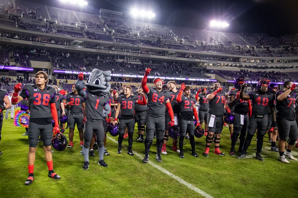 Photograph of TCU football players reciting the school alma matter on the field of Amon G. Carter Stadium in Fort Worth, Texas. SuperFrog joins them, holding up the “Go Frogs” hand sign.