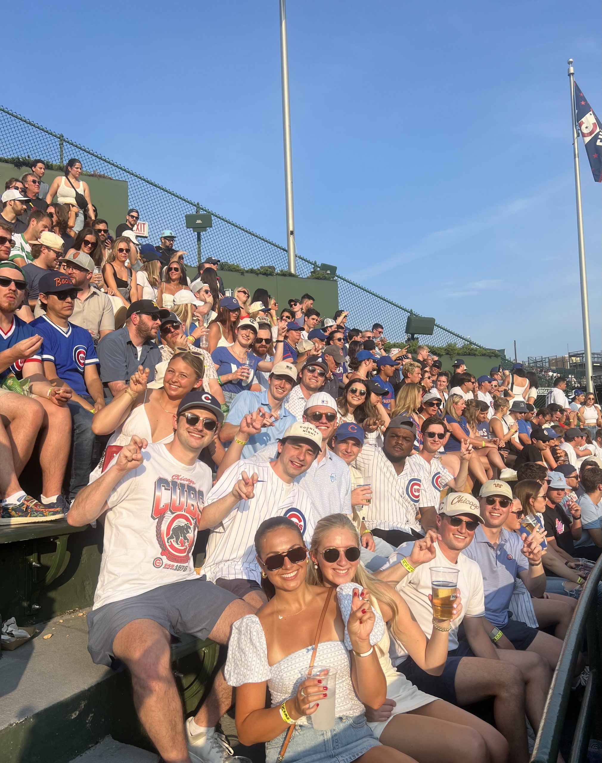 Photograph of a group seated in the stands at Wrigley Stadium in Chicago, taking in a Cubs game. Several members of the group are flashing the "Go Frogs" hand sign.