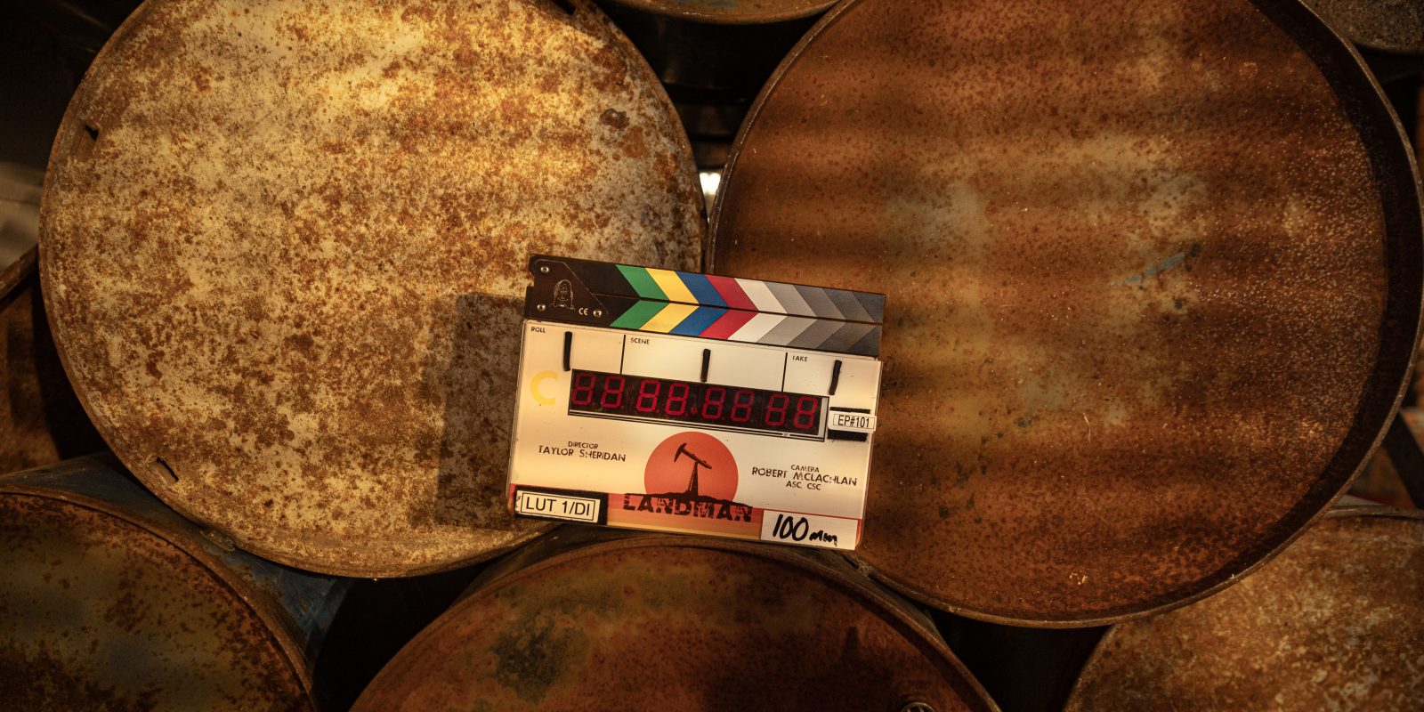 A photograph of a film slate place on a collection of oil barrels. Soft light streams across the image.