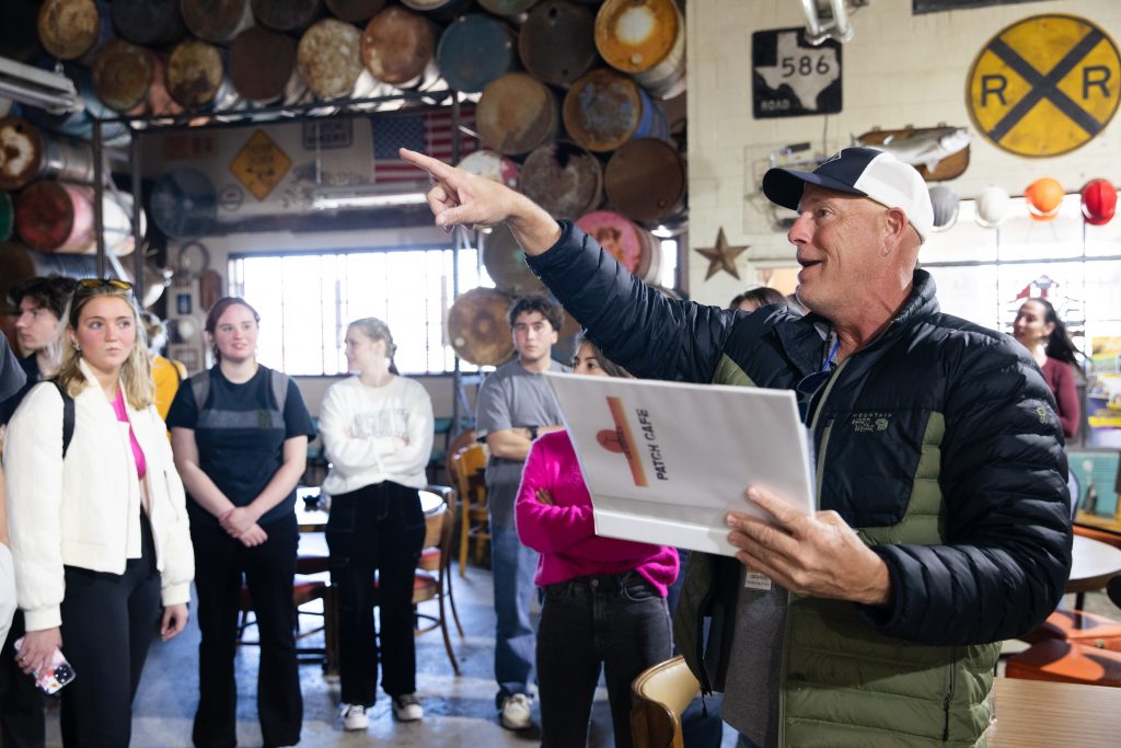 Photograph of a location manager giving college students a tour of a bar set used in the production of the Paramount+ show “Landman.” The location manager points out of frame with their right hand as the students observe.