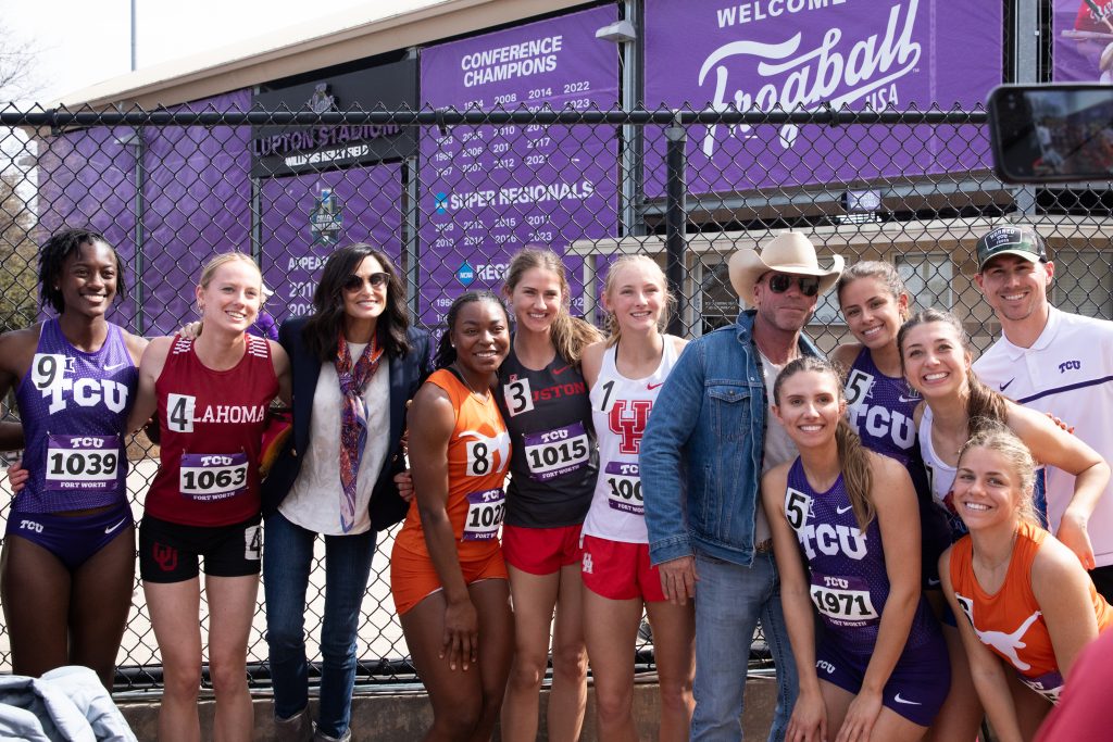 Photograph of roughly a dozen college students clad in track & field uniforms from several Big 12 universities. Among the group stands director Chris Sheridan.