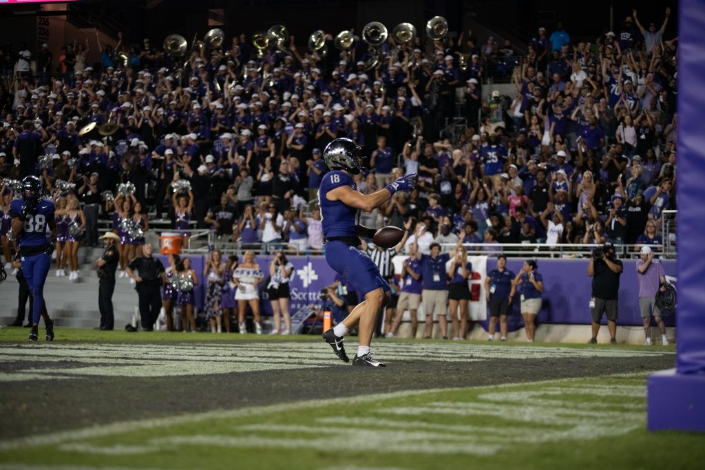 Photograph of TCU wide receiver jack Bech celebrating in the back of the end zone on the field at Amon G. Carter Stadium in Fort Worth, Texas. Bech points to the crowd in reaction to a touchdown catch, as the fans cheer. 