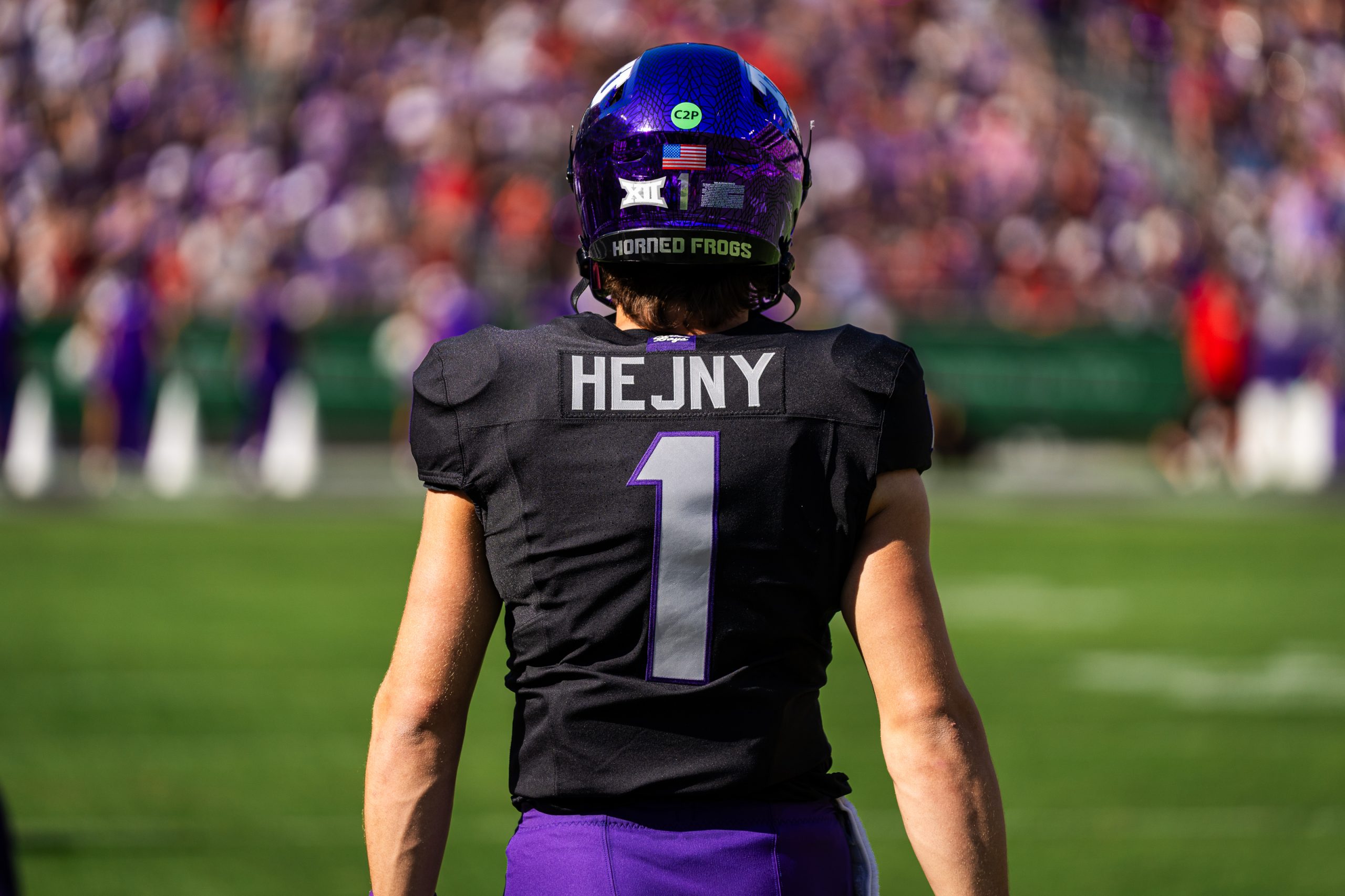 Photograph of TCU quarterback Hauss Hejny, pictured from the rear. Hejny, wearing a purple TCU helmet with a black jersey and purple pants, looks straight ahead.