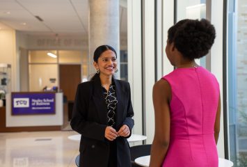 Photograph of TCU student Afrin Shekh facing the camera as she speaks to fellow student, Anaya White, at the Neeley School of Business on the TCU campus.