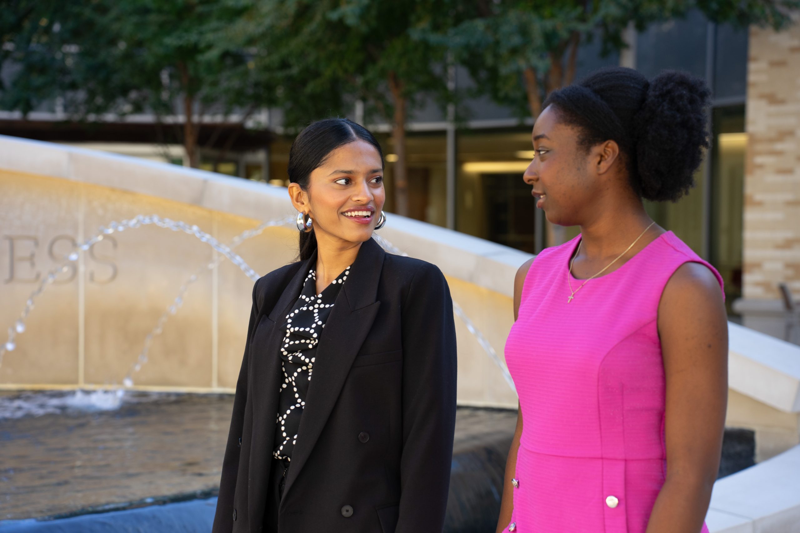 Photograph of TCU student Afrin Shekh facing the camera as she speaks to fellow student, Anaya White, at the Neeley School of Business on the TCU campus.