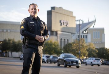 Photograph of Anthony White standing in a parking lot beside Amon G. Carter Stadium with his hands crossed over his stomach.