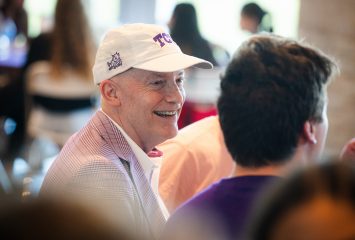 Photograph of Chancellor Victor J. Boschini, Jr., wearing a white TCU baseball hat, dress shirt and light purple blazer as he chats with members of the Class of 2028 during the Frogs First Family Dinner in August 2024.