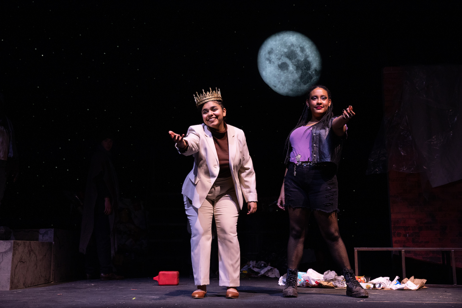 Student actors, including Jessica Willis, are pictured on stage during a production of "Marisol."A full moon sits against a dark background, and the actors have their hands outstretched toward the audience.