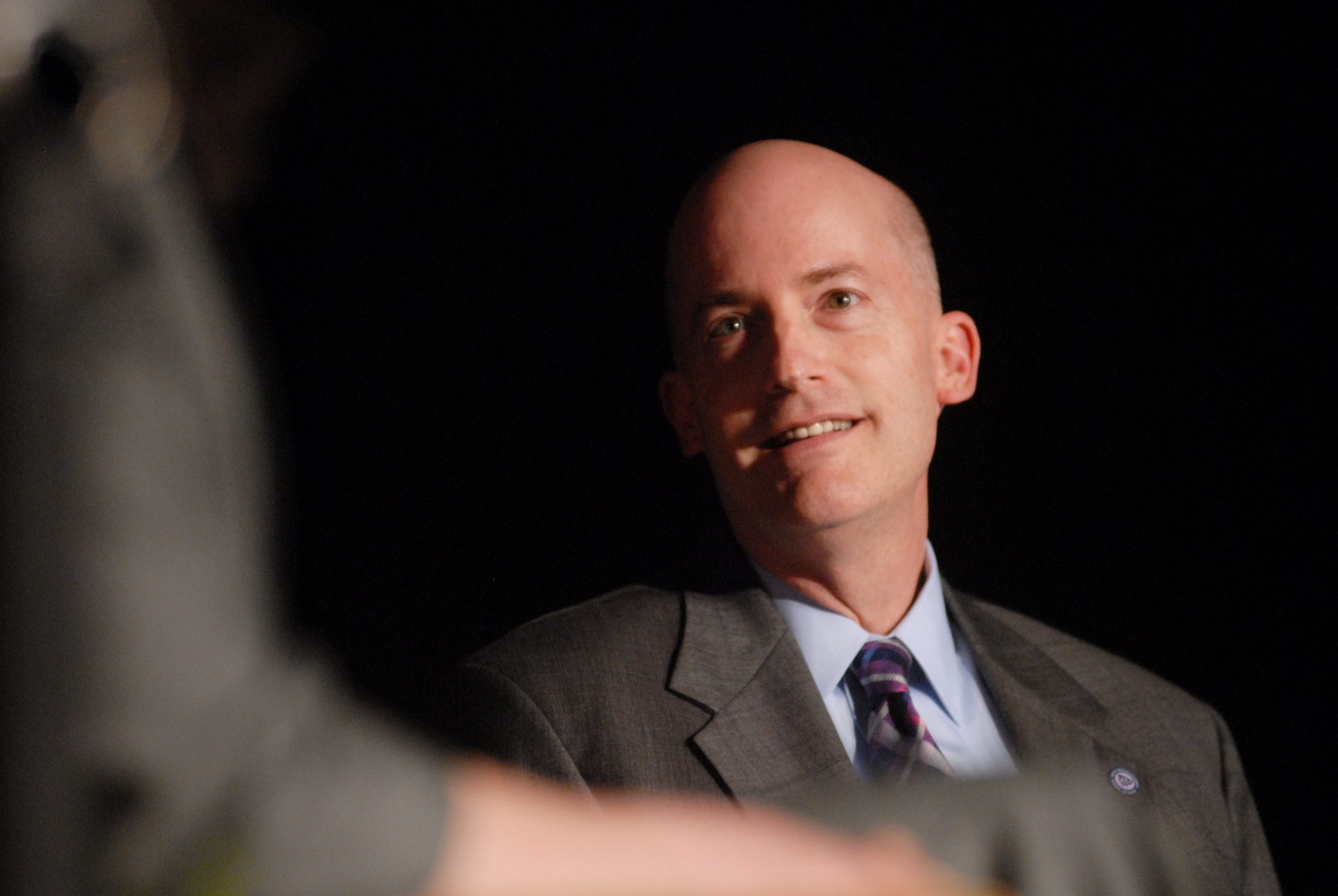 Photograph of Chancellor Victor J. Boschini Jr. in a suit and tie, smiling slightly against a dark background.