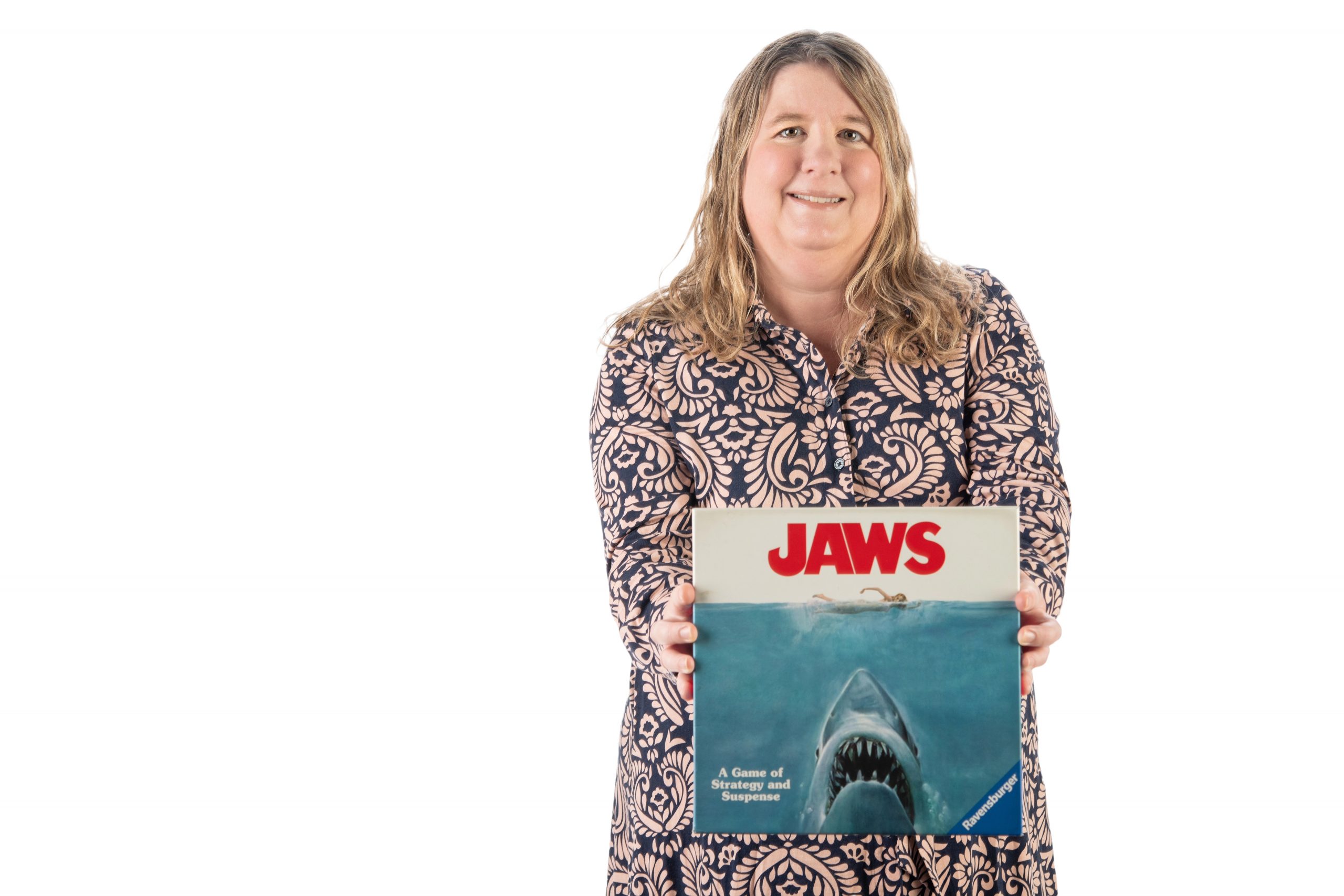 TCU film professor Kim Owczarski holds a 'Jaws'-themed board game while standing against a white backdrop.