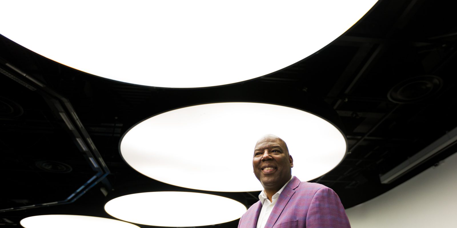 Photograph of TCU alum Carlos Treadway, executive vice president of international at Ford Credit, shot from a low angle with large, bright overhead lights in the background.