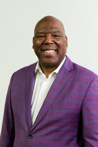 Portrait of TCU alum Carlos Treadway, executive vice president international of Ford Credit, smiling at the camera in a white dress shirt and a purple and light blue grid-patterned blazer.